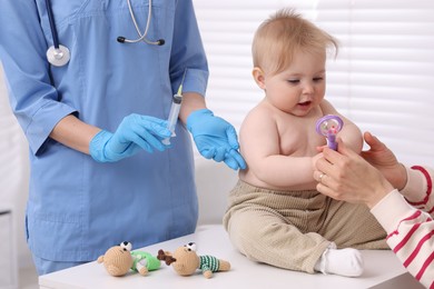 Photo of Mother and her cute baby having appointment with pediatrician in clinic, closeup. Doctor vaccinating child