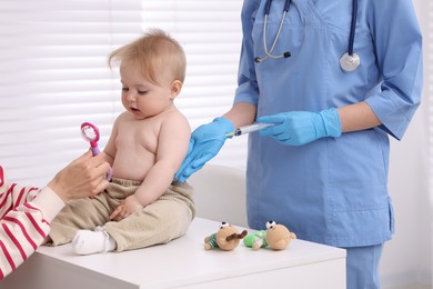 Photo of Mother and her cute baby having appointment with pediatrician in clinic, closeup. Doctor vaccinating child