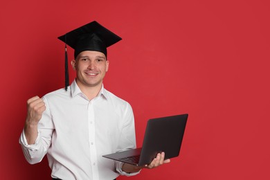 Photo of Happy student with laptop after graduation on red background. Space for text