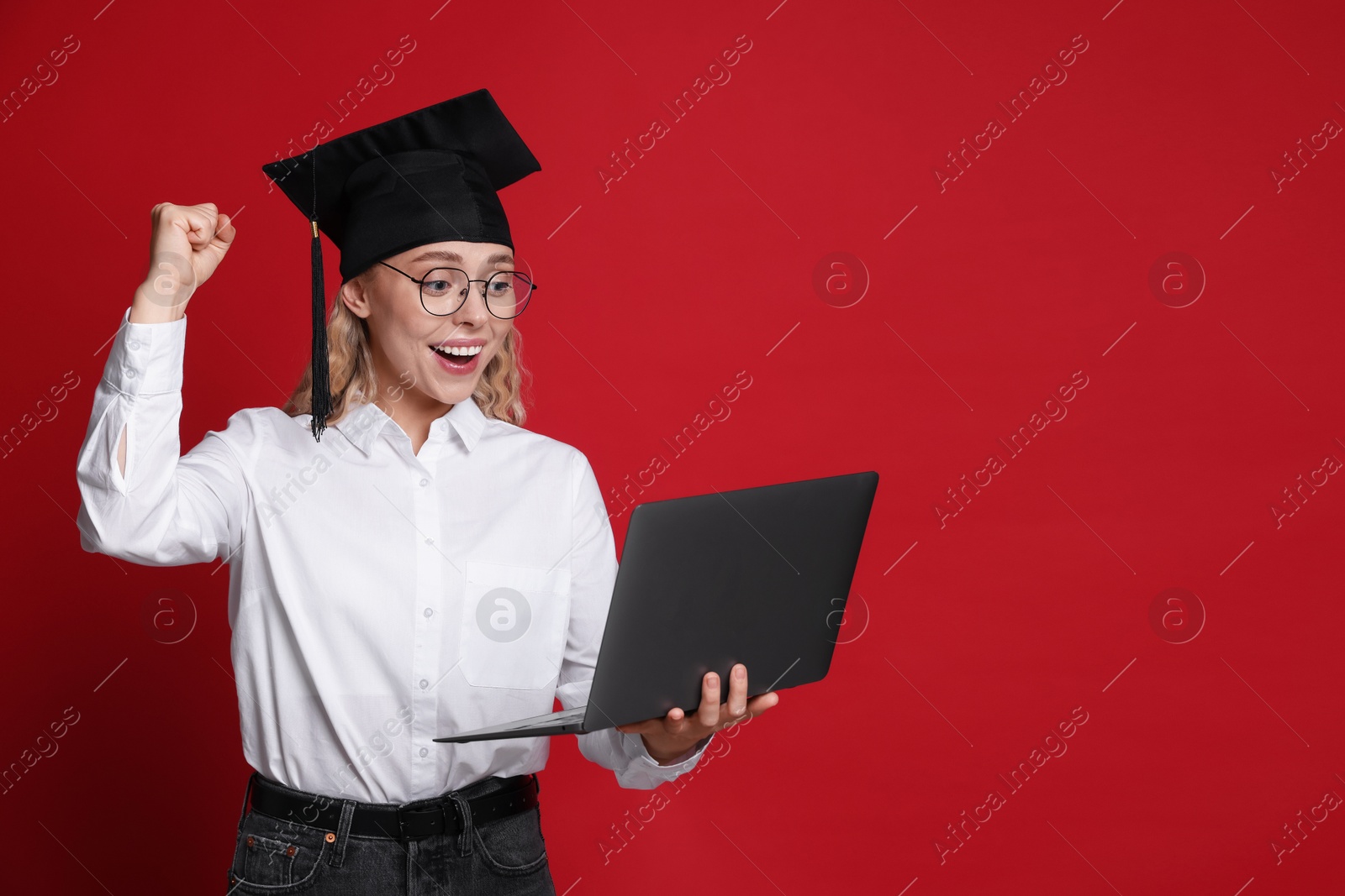 Happy student with laptop after graduation on red background. Space for text Photo of Happy student with laptop after graduation on red background. Space for text