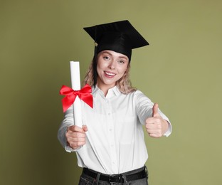 Photo of Happy student with diploma showing thumbs up after graduation on green background