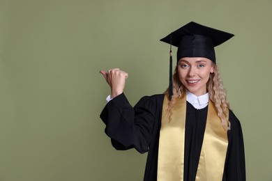 Photo of Happy student pointing at something after graduation on green background. Space for text