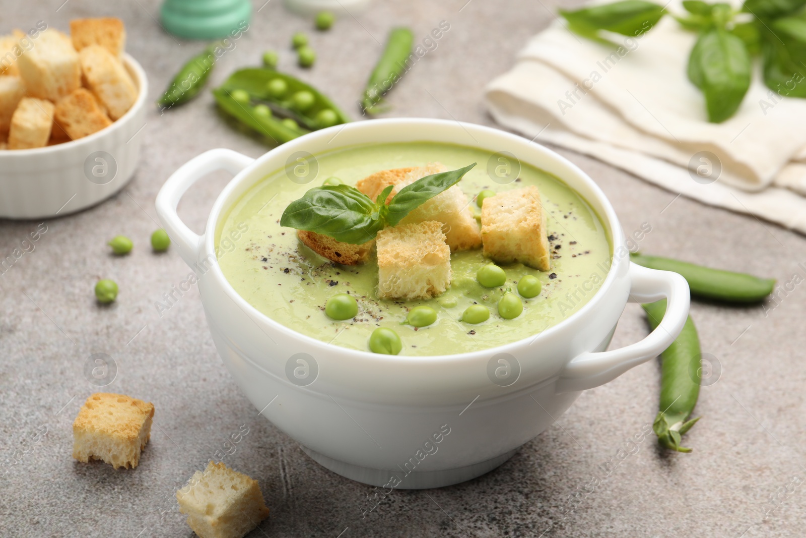 Tasty pea cream soup with croutons and basil served on grey table, closeup Photo of Tasty pea cream soup with croutons and basil served on grey table, closeup