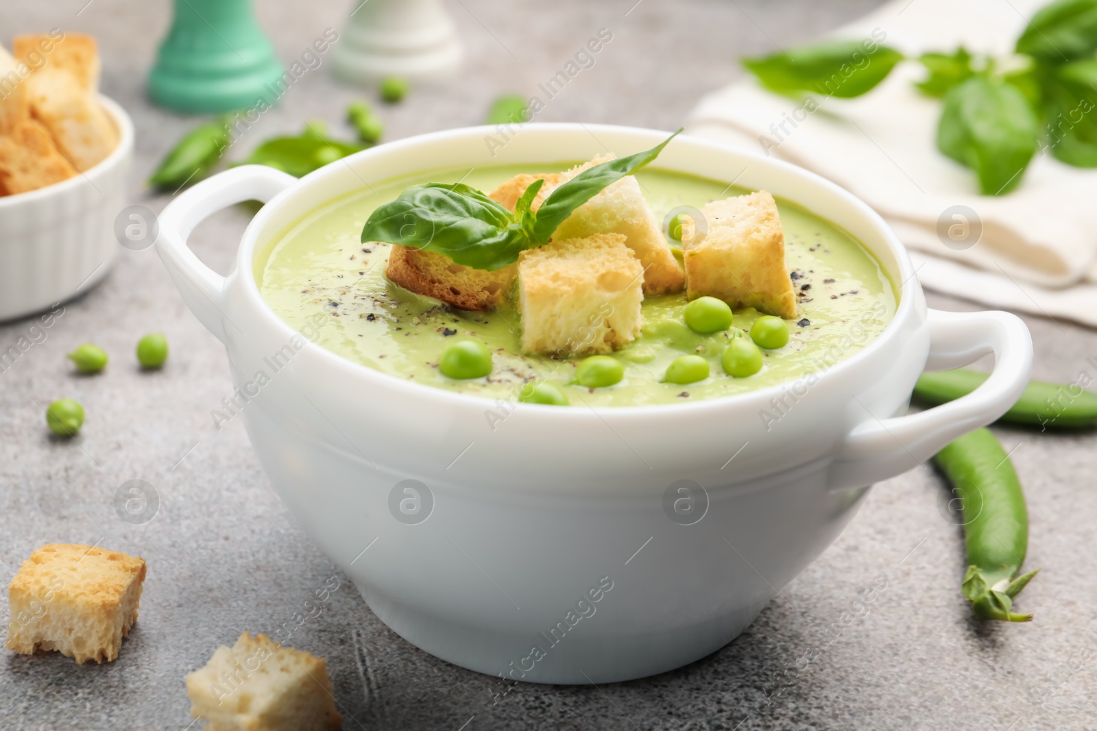 Tasty pea cream soup with croutons and basil served on grey table, closeup Photo of Tasty pea cream soup with croutons and basil served on grey table, closeup