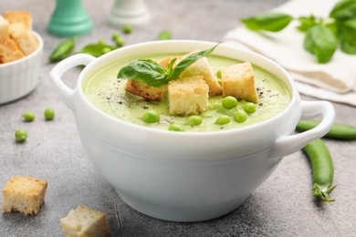 Photo of Tasty pea cream soup with croutons and basil served on grey table, closeup