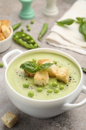 Photo of Tasty pea cream soup with croutons and basil served on grey table, closeup