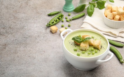 Photo of Tasty pea cream soup with croutons and basil served on grey table. Space for text