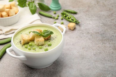 Photo of Tasty pea cream soup with croutons and basil served on grey table. Space for text
