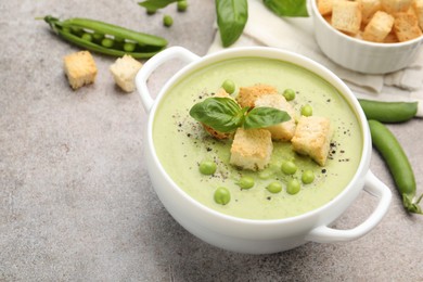 Photo of Tasty pea cream soup with croutons and basil served on grey table, closeup
