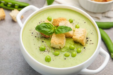 Photo of Tasty pea cream soup with croutons and basil served on grey table, closeup