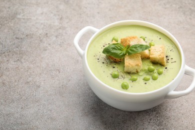 Photo of Tasty pea cream soup with croutons and basil on grey table, closeup. Space for text