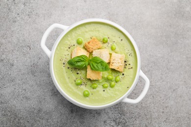 Photo of Tasty pea cream soup with croutons and basil on grey table, top view