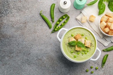 Photo of Tasty pea cream soup with croutons and basil served on grey table, flat lay. Space for text