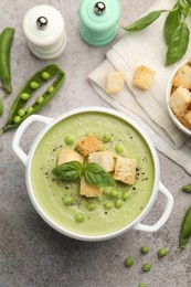 Photo of Tasty pea cream soup with croutons and basil served on grey table, flat lay