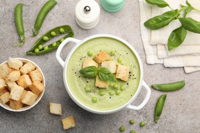 Photo of Tasty pea cream soup with croutons and basil served on grey table, flat lay