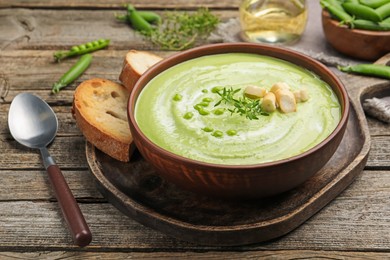 Photo of Tasty pea cream soup with croutons and thyme served on wooden table, closeup