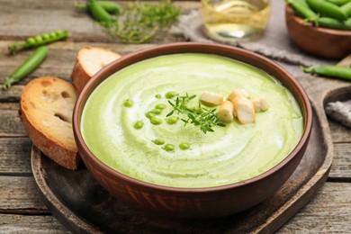 Photo of Tasty pea cream soup with croutons and thyme served on wooden table, closeup