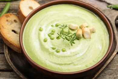 Photo of Tasty pea cream soup with croutons and thyme served on wooden table, closeup