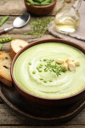 Photo of Tasty pea cream soup with croutons and thyme served on wooden table, closeup