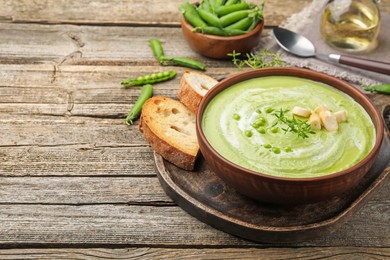 Photo of Tasty pea cream soup with croutons and thyme served on wooden table. Space for text