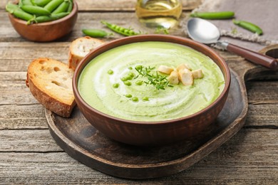 Photo of Tasty pea cream soup with croutons and thyme served on wooden table, closeup