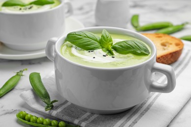 Photo of Tasty pea cream soup with basil served on white marble table, closeup