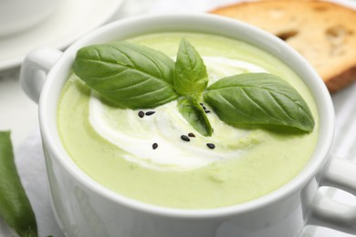 Photo of Tasty pea cream soup with basil served on white table, closeup