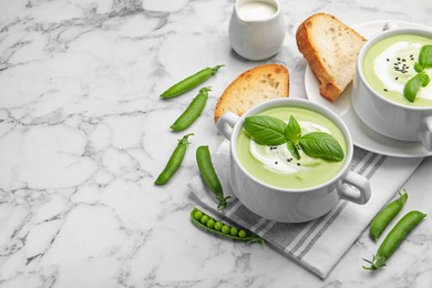 Photo of Tasty pea cream soup with basil served on white marble table. Space for text
