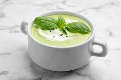 Photo of Tasty pea cream soup with basil served on white marble table, closeup