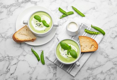 Photo of Tasty pea cream soup with basil served on white marble table, flat lay