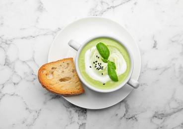 Photo of Tasty pea cream soup with basil served on white marble table, top view