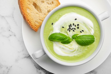 Photo of Tasty pea cream soup with basil served on white marble table, top view