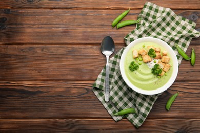 Photo of Tasty pea cream soup with croutons and broccoli served on wooden table, flat lay. Space for text