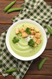 Photo of Tasty pea cream soup with croutons and broccoli served on wooden table, flat lay