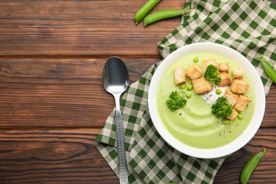 Photo of Tasty pea cream soup with croutons and broccoli served on wooden table, flat lay. Space for text