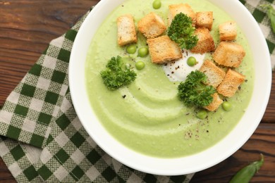 Photo of Tasty pea cream soup with croutons and broccoli served on wooden table, top view