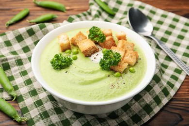 Photo of Tasty pea cream soup with croutons and broccoli served on wooden table, closeup