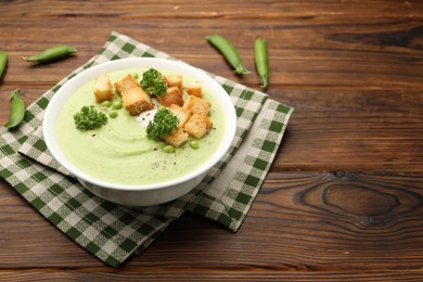 Photo of Tasty pea cream soup with croutons and broccoli served on wooden table. Space for text