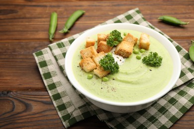 Photo of Tasty pea cream soup with croutons and broccoli served on wooden table, closeup