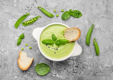 Photo of Tasty pea cream soup with basil and crouton served on grey table, flat lay