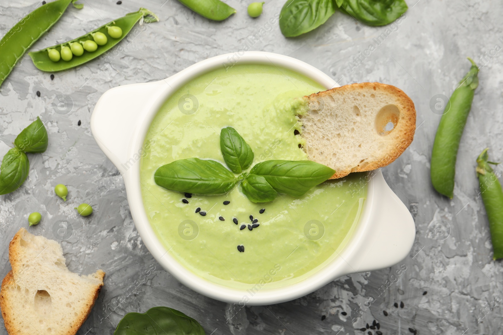 Tasty pea cream soup with basil and crouton served on grey table, flat lay Photo of Tasty pea cream soup with basil and crouton served on grey table, flat lay