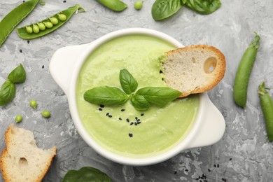 Photo of Tasty pea cream soup with basil and crouton served on grey table, flat lay