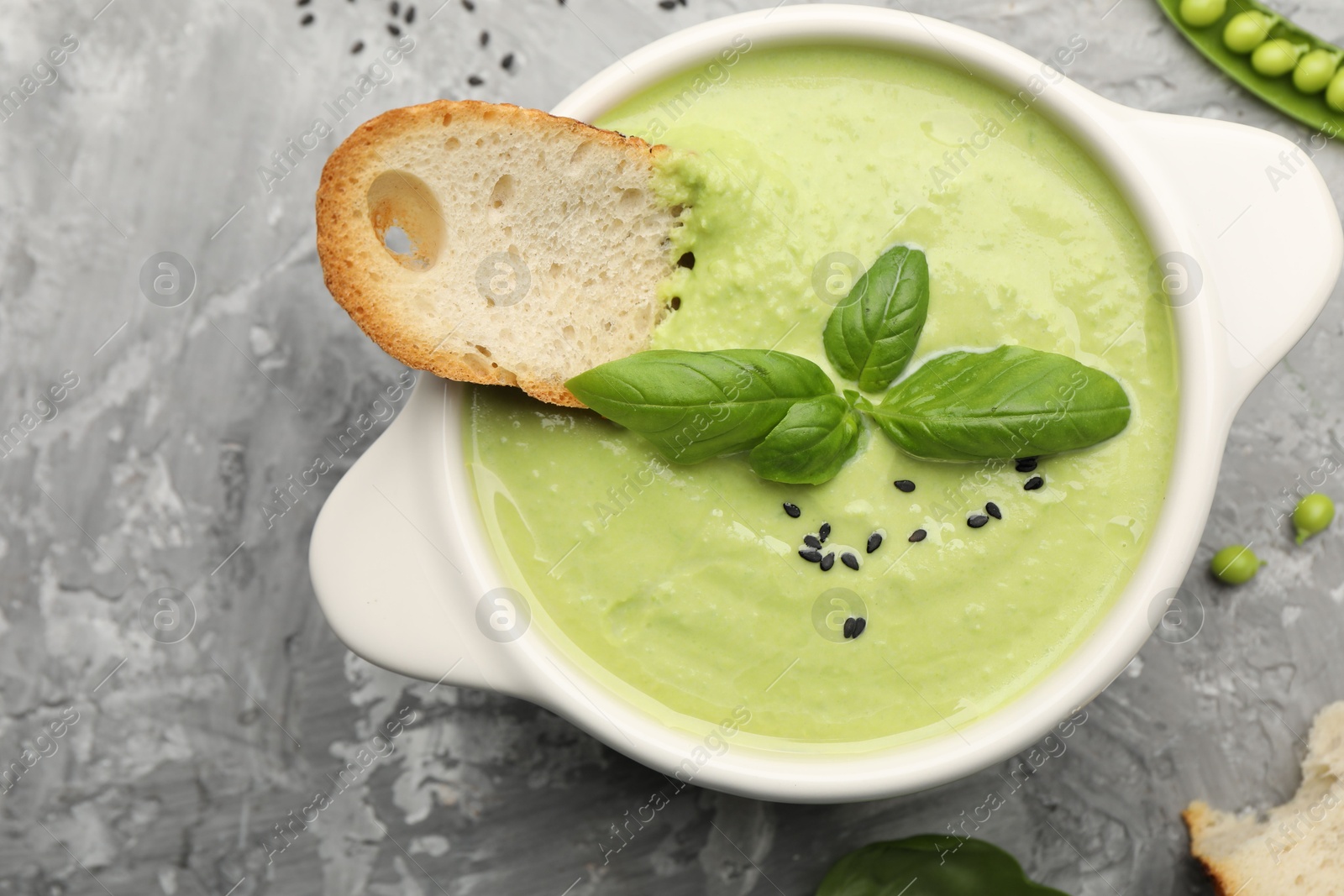Tasty pea cream soup with basil and crouton served on grey table, flat lay Photo of Tasty pea cream soup with basil and crouton served on grey table, flat lay