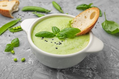 Photo of Tasty pea cream soup with basil and crouton served on grey table, closeup
