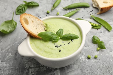Photo of Tasty pea cream soup with basil and crouton served on grey table, closeup