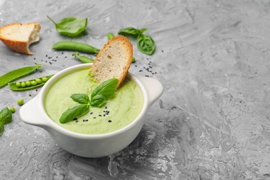 Photo of Tasty pea cream soup with basil and crouton served on grey table. Space for text