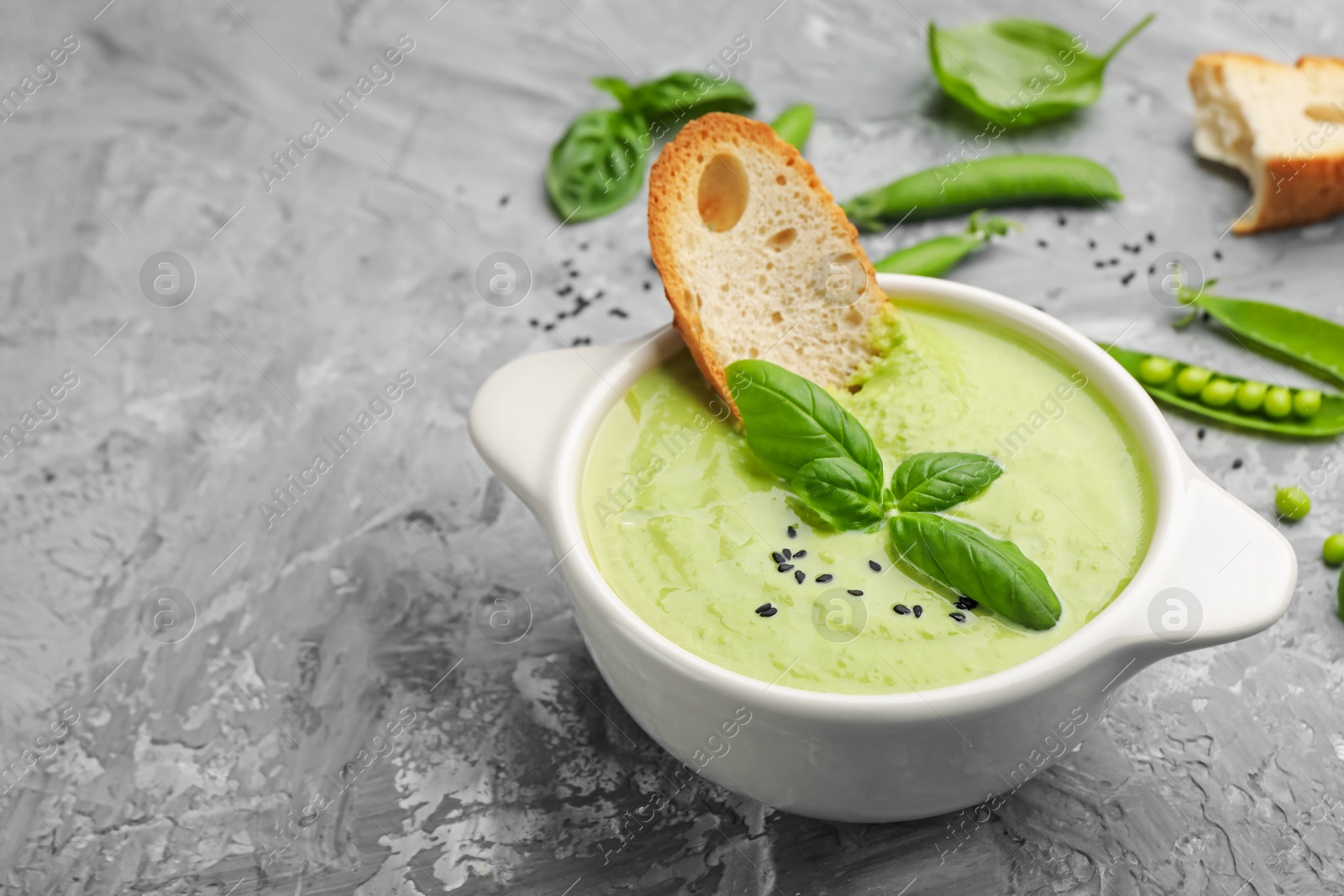 Tasty pea cream soup with basil and crouton served on grey table, closeup. Space for text Photo of Tasty pea cream soup with basil and crouton served on grey table, closeup. Space for text