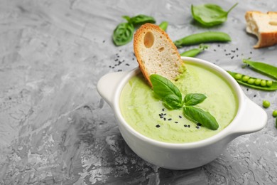 Photo of Tasty pea cream soup with basil and crouton served on grey table, closeup. Space for text