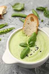 Photo of Tasty pea cream soup with basil and crouton served on grey table, closeup