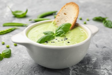 Photo of Tasty pea cream soup with basil and crouton served on grey table, closeup